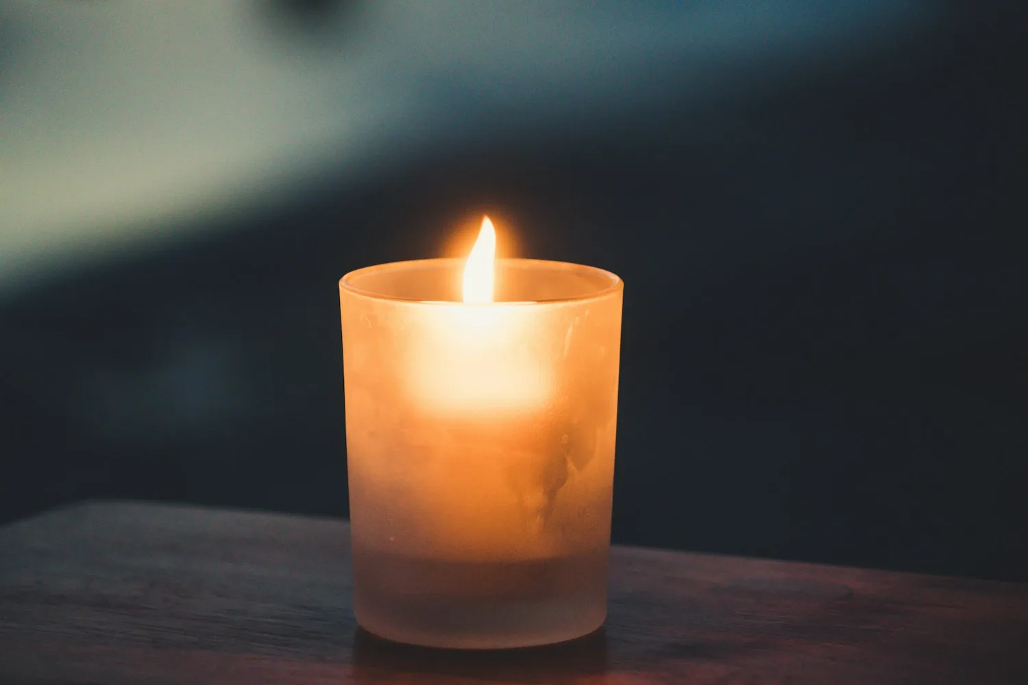 A single lit candle in a frosted glass holder on a wooden surface